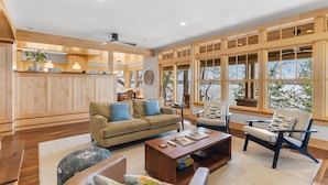 A spacious living area with a wooden ceiling, large windows, and a kitchen in the background. - Turtle Lake Cottage (Shoreview)