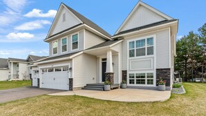A modern two-story house with a garage, a stone accent wall, and a well-maintained lawn. - Savanna Grove (Blaine)