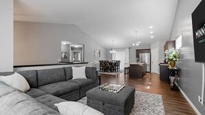A modern living room with a grey sectional sofa, ottoman, and dining area with a table and chairs. - Savanna Grove (Blaine)