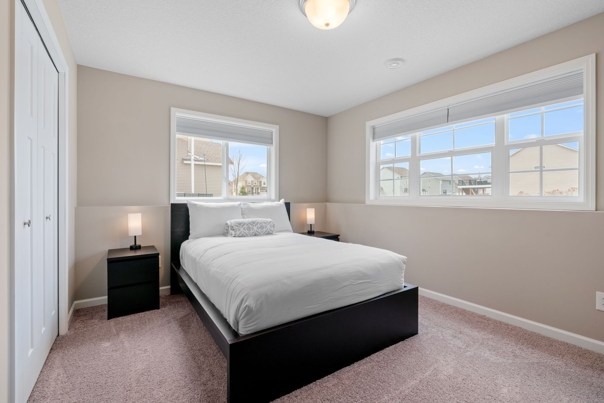 A bedroom with a bed, two bedside tables, a window, and a door.