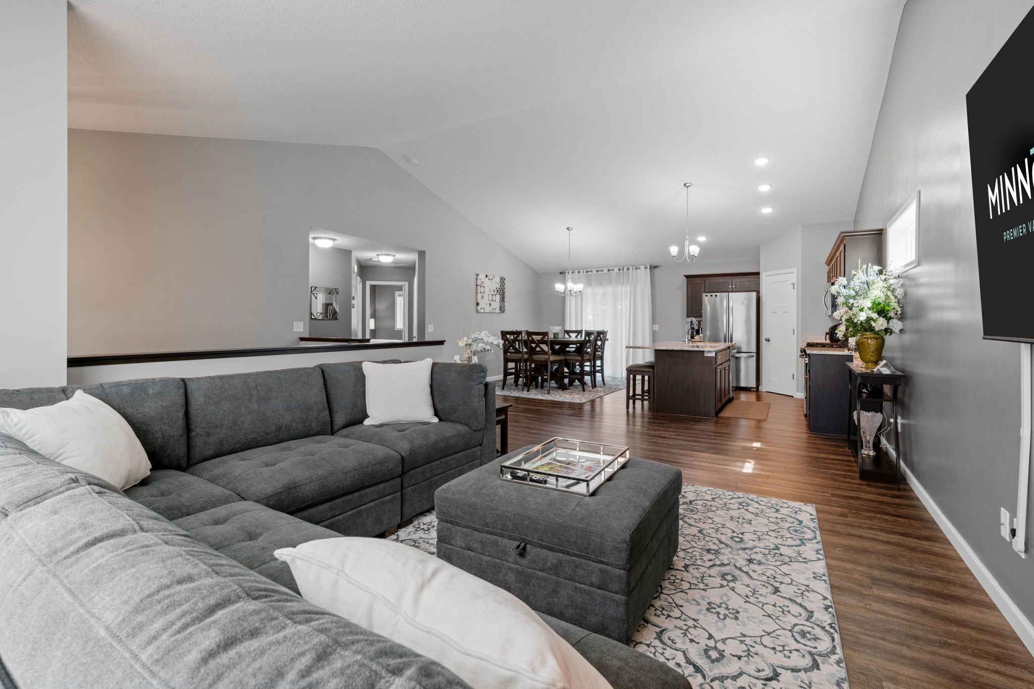 A modern living room with a grey sectional sofa, ottoman, and dining area with a table and chairs.