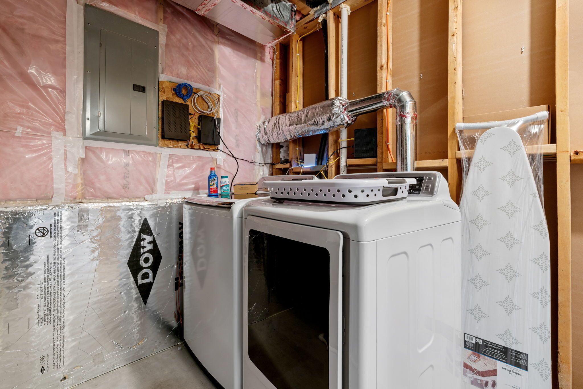 Een kamer in aanbouw, met blootgelegd isolatiemateriaal, een wasmachine en een droger.