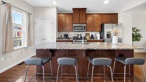 Una cocina con encimera de granito, electrodomésticos de acero inoxidable, armarios de madera y una zona de bar con taburetes.