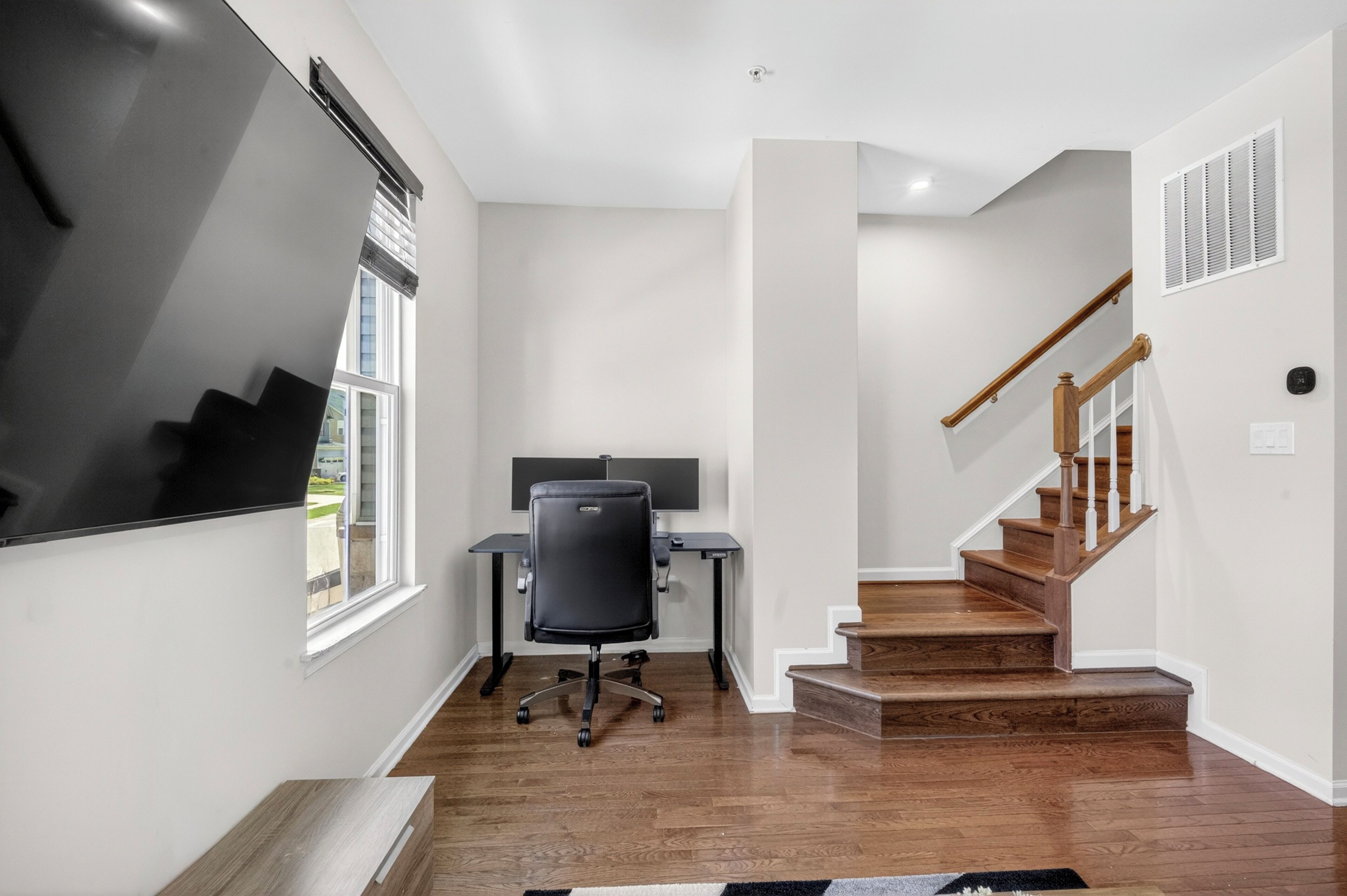 A modern interior with a staircase, a desk with a chair, and a large window.