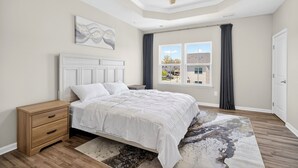 Un dormitorio con cama, mesita de noche, ventilador de techo, ventana con cortinas y vistas a edificios.