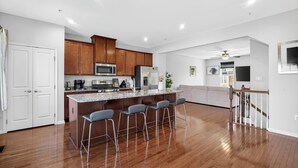 Una cocina moderna con armarios de madera, una isla central con taburetes y un comedor con una escalera.