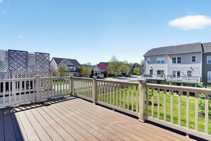 A wooden deck with a white railing, a view of residential buildings, and a clear sky.