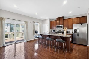 A modern kitchen with a central island, bar stools, stainless steel appliances, and a sliding glass door to a balcony.