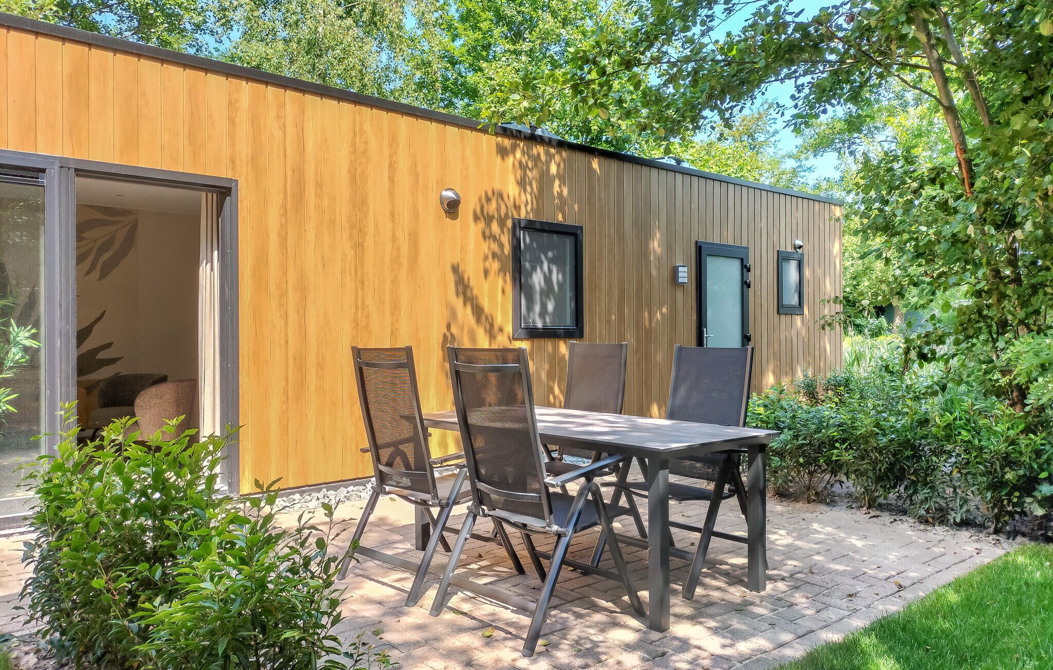 Una cabaña de madera moderna con un patio, dos sillas y una mesa.