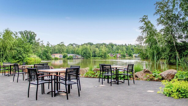 An outdoor patio with tables and chairs, overlooking a lake with houses in the background. - Nice home in Oosterwolde with WiFi (Oosterwolde)