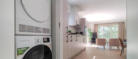 A modern kitchen with a built-in washer and dryer, a dining area with two chairs, and a large window with curtains.