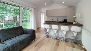 Et moderne køkken med en bar, en grå sofa og udsigt til grøn vegetation udenfor.