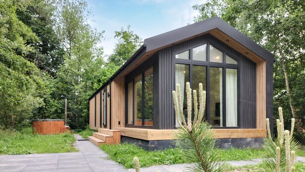 En moderne hytte med store vinduer, en træterrasse og en omkringliggende skov.