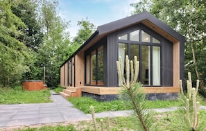 Una cabaña moderna de madera con ventanas amplias, una terraza de madera y un bosque circundante.