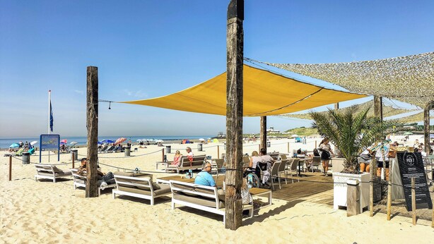 Un café frente al mar con terraza, una playa de arena y sombrillas que dan sombra.