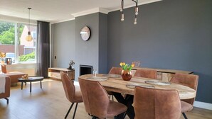Un comedor moderno con una mesa redonda de madera, seis sillas acolchadas y un jarrón con tulipanes.
