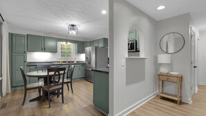 Een moderne keuken met groene kastjes, een roestvrijstalen koelkast en een eethoek met een houten tafel en stoelen.