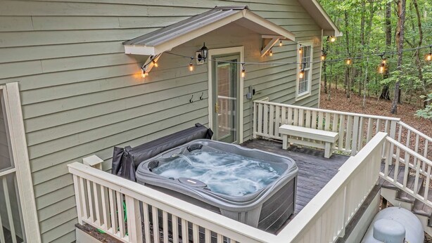 Een hottub op een houten terras met een witte reling, omringd door bomen.