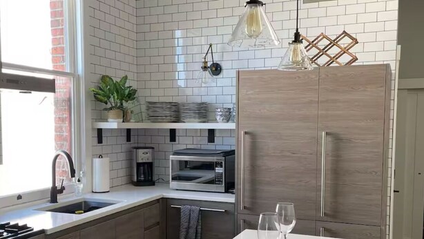 A modern kitchen with a central island, stainless steel appliances, and a brick backsplash.