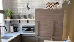 A modern kitchen with white subway tiles, a built-in microwave, a stainless steel refrigerator, wooden cabinets, and a hanging pendant light.