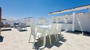 Une terrasse sur le toit avec une table et des chaises blanches, un bar intégré et un ciel d’un bleu limpide.