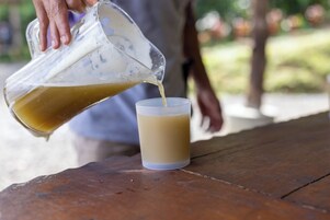 Una persona sirve un líquido de una jarra transparente en un vaso sobre una mesa de madera.