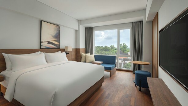 Una camera d'albergo moderna con un letto grande, un angolo salotto con un tavolino, un'ampia finestra con tende e una televisione a schermo piatto.