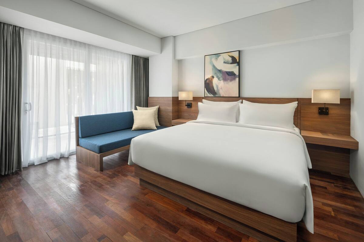 A modern hotel room with a large bed, a sofa, and a large window with curtains.