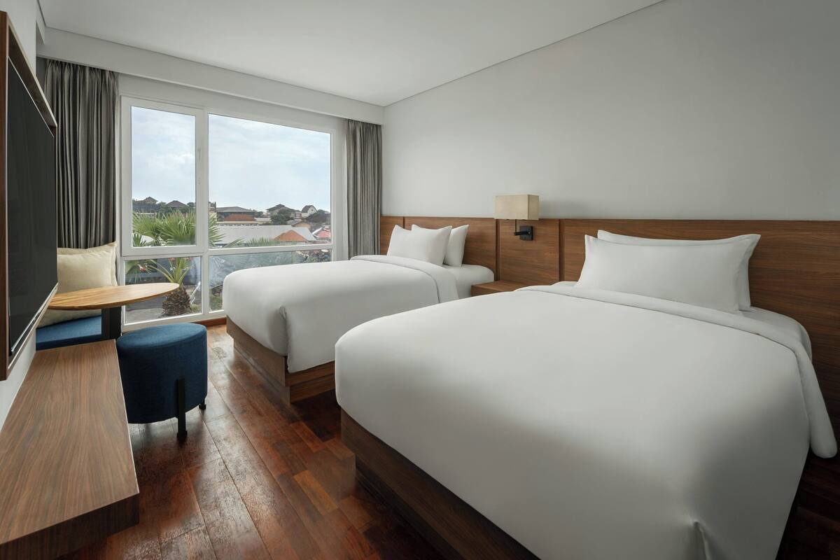 A hotel room with two beds, a desk, and a view of the city.