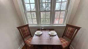 Mesa de comedor con cuatro sillas, lista para cuatro comensales, ubicada frente a una ventana con vistas a árboles y edificios.