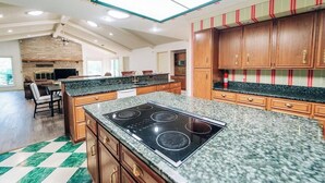 A spacious kitchen with granite countertops, wooden cabinets, and a central island with a stovetop.