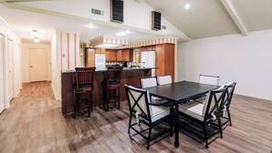 A spacious kitchen with wooden cabinets, a central island with bar stools, and a dining table with chairs.