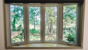 A bay window with a view of a backyard with trees and a wooden deck.