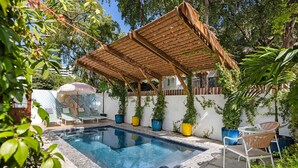 A swimming pool with a wooden pergola, lounge chairs, and potted plants. - Oasis Condado Pool Parking Beach Steps Away (San Juan)