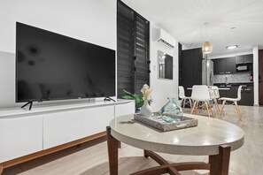 A modern living room with a flat-screen TV, a dining table, and a kitchen area in the background. - Ocean Park Oasis Steps to Beach Private Parking (San Juan)