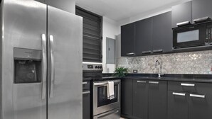 A modern kitchen with stainless steel appliances, dark cabinetry, and a hexagonal tile backsplash. - Ocean Park Oasis Steps to Beach Private Parking (San Juan)