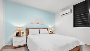 A bedroom with a bed, nightstands, a wall-mounted air conditioner, and a window with blinds. - Ocean Park Oasis Steps to Beach Private Parking (San Juan)