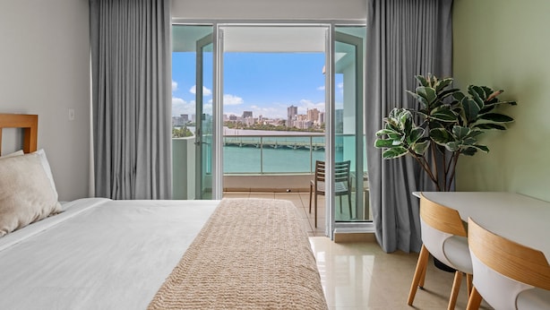A hotel room with a bed, a dining table, a chair, a potted plant, and a balcony with a city view. - Oceanfront Old San Juan Charm Private Rooftop (San Juan)