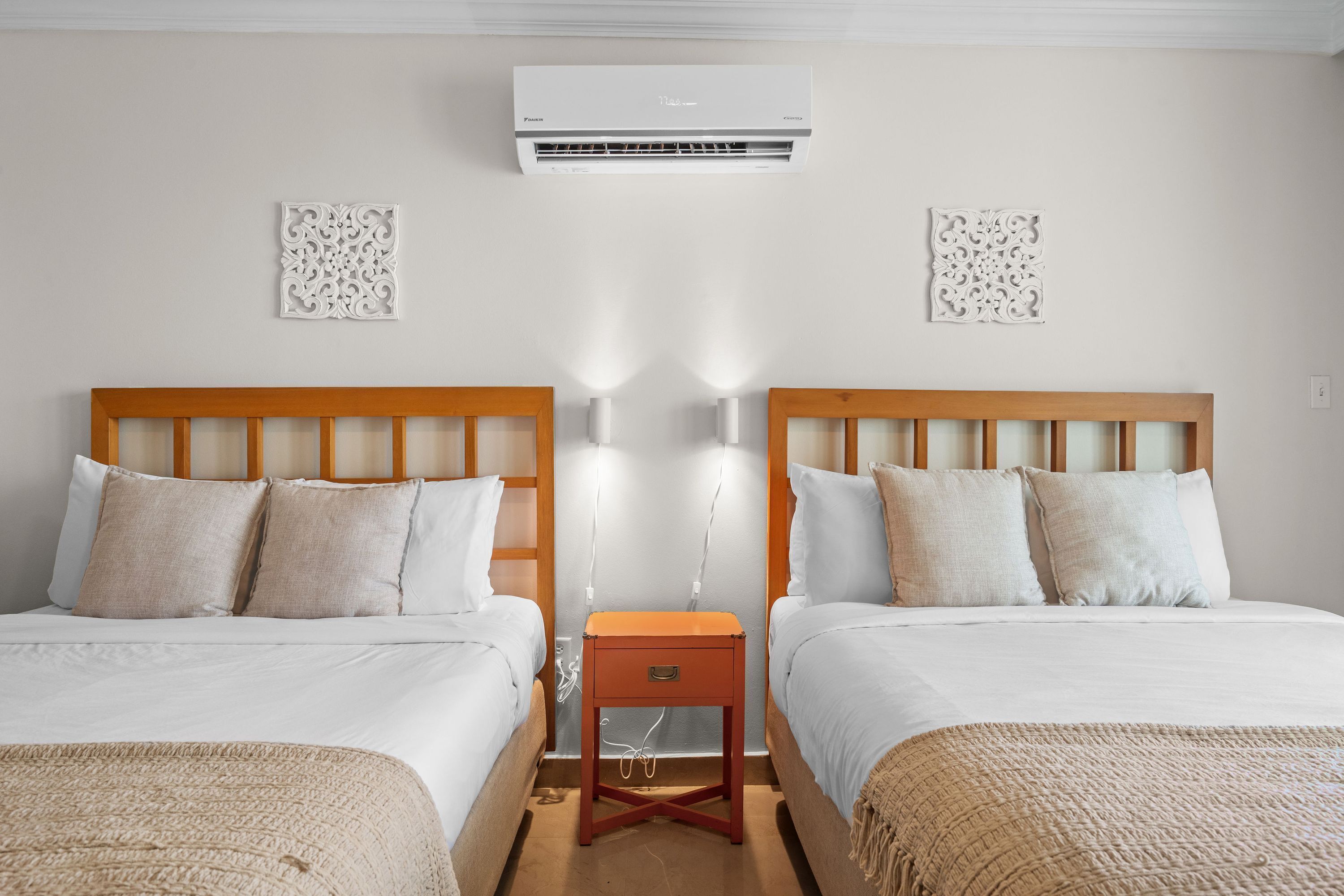 Camera d'albergo con due letti, un comodino, un condizionatore d'aria e elementi decorativi a parete.