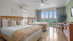 A hotel room with two beds, a ceiling fan, a desk with chairs, and a large window with a view of the city. - Oceanfront Old San Juan Charm Private Rooftop (San Juan)
