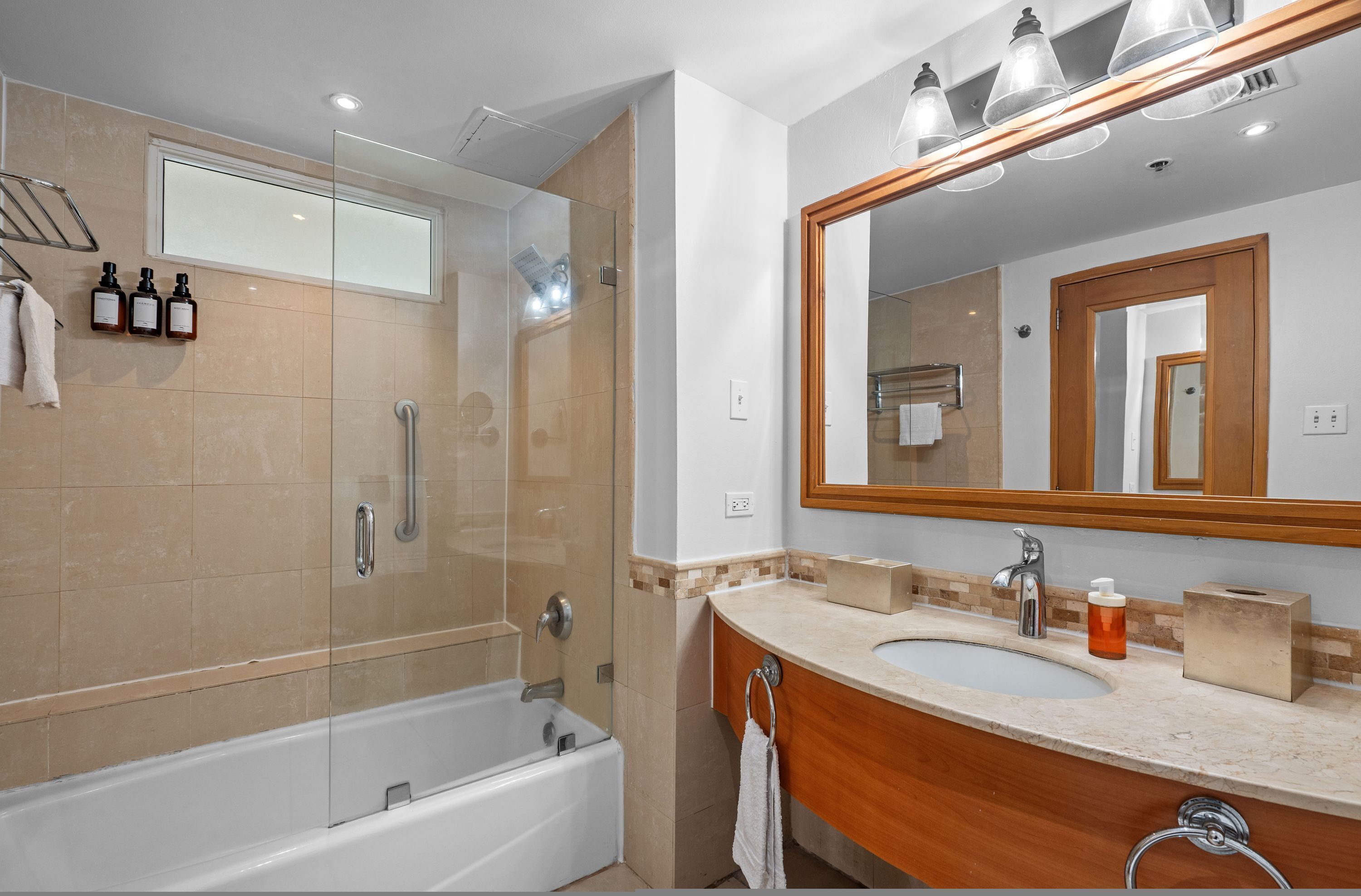 A modern bathroom with a glass-enclosed shower, a large mirror, and a vanity with a sink and toiletries.