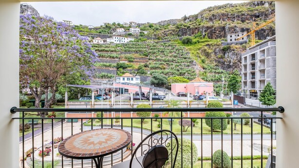 Un balcón con una mesa y una silla, con vistas a una colina con edificios y una grúa de construcción.