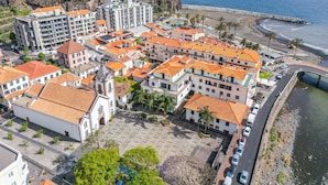 Un pueblo costero con edificios de tejados terracota, una plaza central y vista al mar.