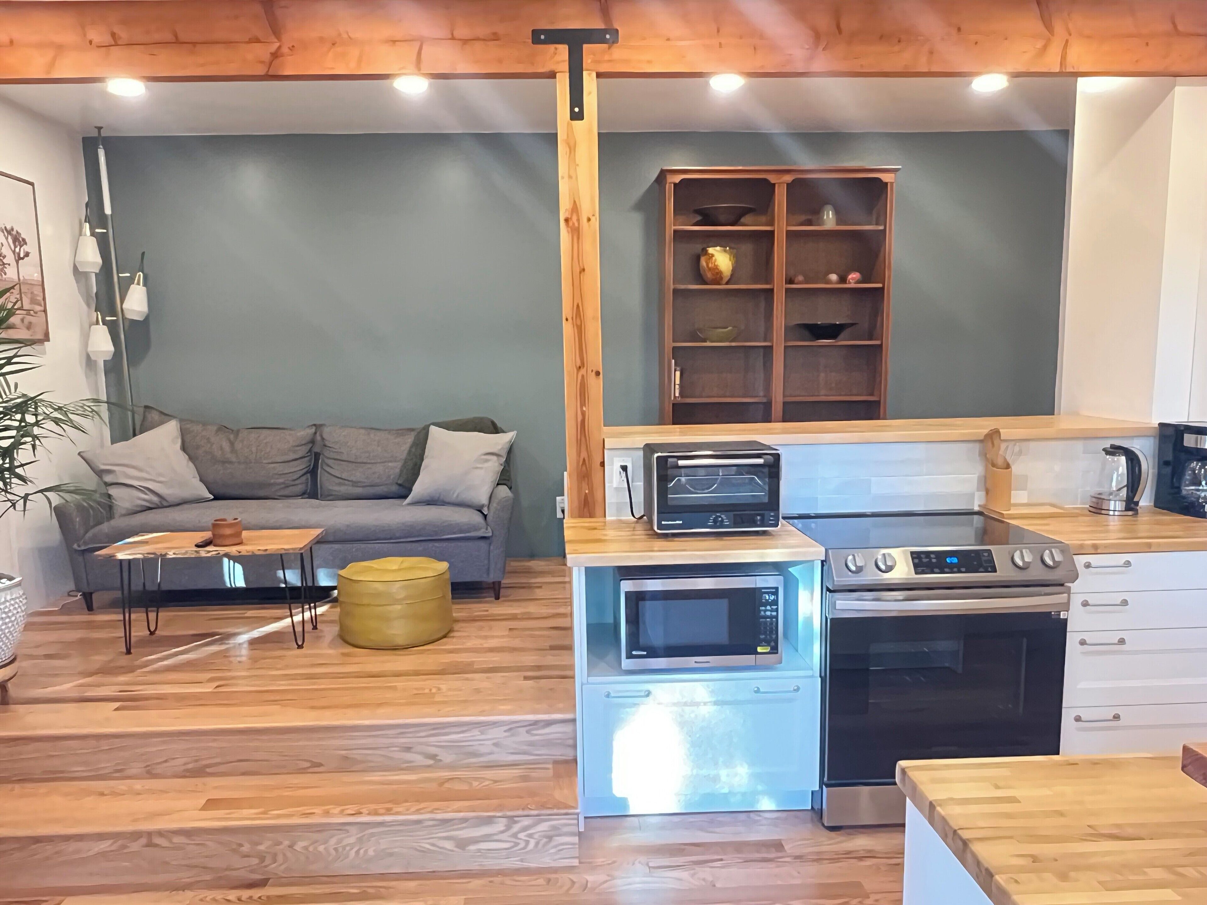 A compact living space with a kitchenette, a grey sofa, a wooden coffee table, and a small plant.