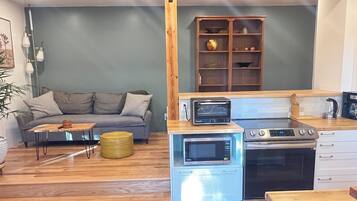 A compact living space with a kitchenette, a grey sofa, a wooden coffee table, and a small plant.