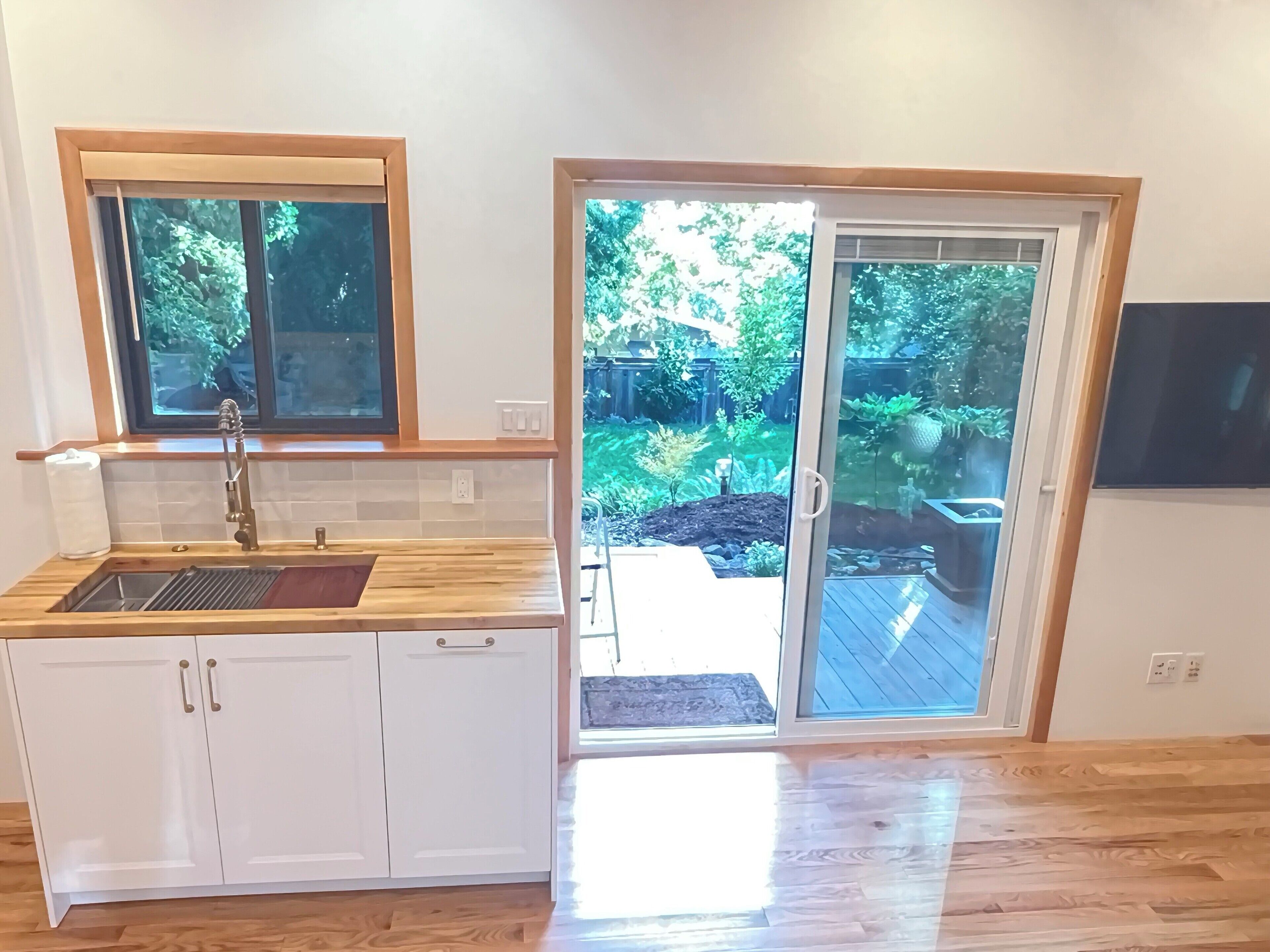 A kitchen with a wooden countertop, a sink, and a window overlooking a garden.