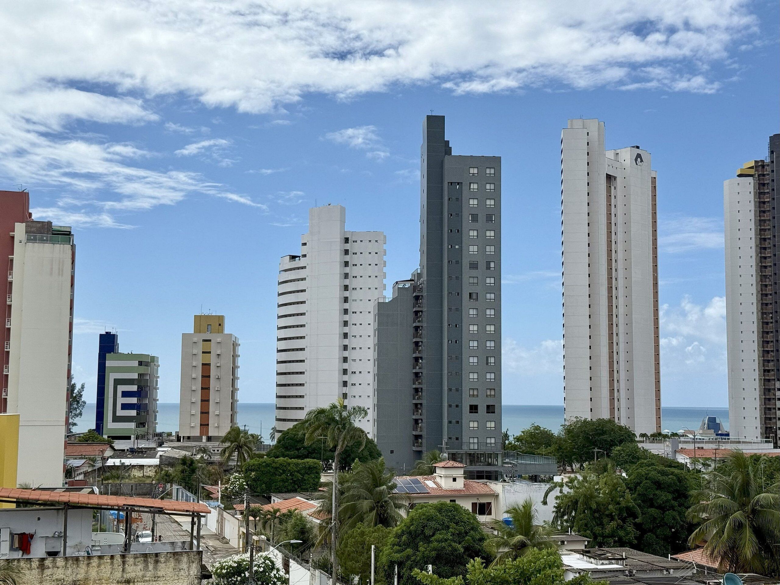 A cityscape with tall buildings, including a prominent skyscraper with a unique design, and a view of the sea.