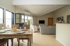 A spacious living area with a dining table set for four, a grey sofa, and a television mounted on the wall. - Mv Lodge (La Couarde-sur-Mer)