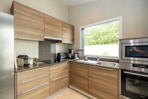 A modern kitchen with wooden cabinets, a stainless steel oven, and a window providing natural light. - Mv Lodge (La Couarde-sur-Mer)