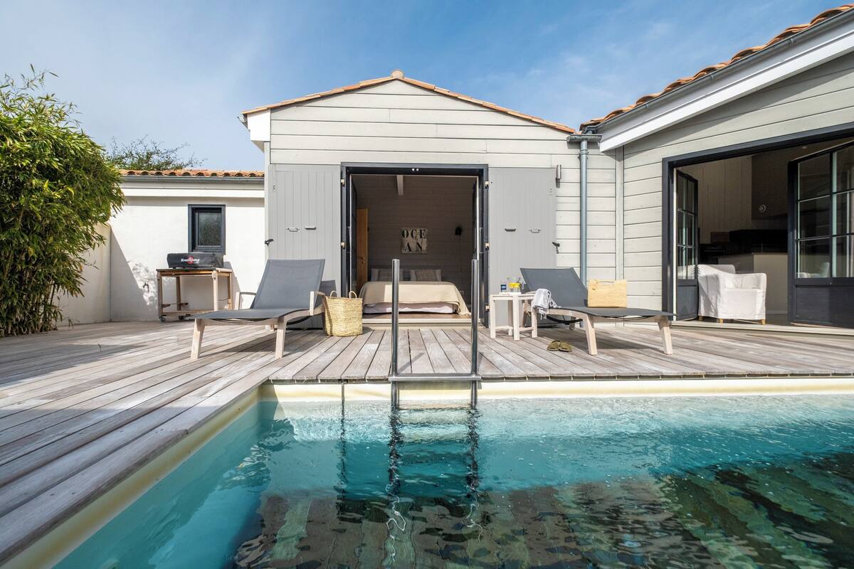 Un espace aménagé au bord de la piscine, avec une terrasse en bois, des chaises longues et une petite table.